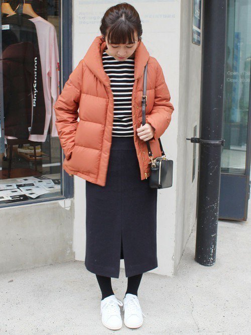 モノトーンコーデにサーモンピンクのダウンジャケットを着た女性